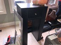 Black wooden pedestal table with one drawer, showing side and drawer front with round metallic knob.