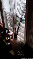 Full view of the tall white vase filled with long decorative branches placed next to a window.