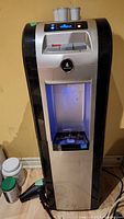 Full view of the tall silver and black Vitapur water cooler with built-in blue light in dispensing area.