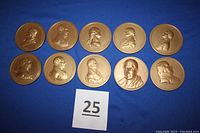 Top-down photo showing all 10 bronze medallions laid flat on blue cloth background, each with a visible profile bust of a president.