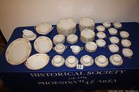 Full view of the Noritake china set placed on a blue tablecloth with the Historical Society logo, showing arrangement of platters, plates, bowls, cups, and serving pieces