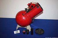 Red Edmund Scientific Astroscan 2001 telescope with two eyepieces and lens cap placed in front on blue surface