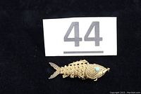 Full view of articulated koi fish pendant with blue turquoise eyes and detailed filigree scales and fins on a black background.