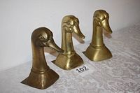 Three brass mallard duck head bookends, patina visible, arranged side by side on a table.