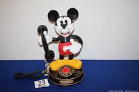 Front view showing Mickey Mouse holding the handset and the push button dial base with gold trim.