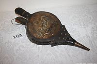 Full view of vintage fireplace bellows showing leather body, brass or copper medallion with medieval scene, and wooden handles.