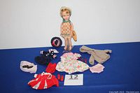 Penny Brite doll standing with all included accessories and extra outfits laid around her including hats, shoes, and clothing pieces.