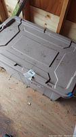 Gray plastic storage tote with lid and dust, placed on wooden floor inside a shed.