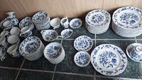 Multiple stacks of white porcelain dinnerware with blue floral pattern arranged on floor. Shows various plates, bowls, cups, saucers.
