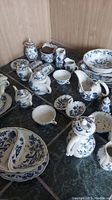 Multiple Blue Danube porcelain serving pieces arranged on a tiled surface against a wooden backdrop, showing tureen, gravy boats, teapots, pitchers, trays, bowls and shakers.