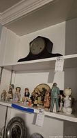 Wooden Waterbury mantel clock on upper shelf above several ceramic figurines and decorative plate