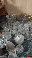 Photo of assorted cut glass bowls, pitchers, and trays arranged on a dark green surface, showing detailed cut glass designs, handles, and various shapes.