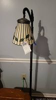 Full view of brass tone metal floor lamp with decorative leaf-patterned glass shade hanging from angled arm.