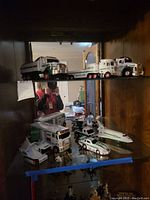 Four Hess trucks with several Hess vehicles including airplane, bus, race car on glass shelf in wooden cabinet, showing the lot's variety