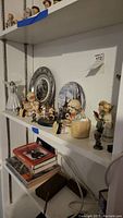Shelf of assorted figurines and decorative plates including Lladro, Goebel carousel horses, and Avon bear figurines