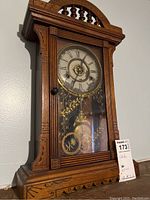 Front view of wooden mantel clock with glass door showing clock face and pendulum inside.