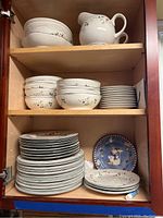 Cabinet shelf with white Pfaltzgraff Winterberry dishes, bowls, plates, and pitchers stacked and arranged inside.