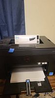 Dell C1660w printer with toner cartridge box placed on top and paper in tray
