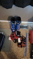 Blue Lange RS70 alpine ski race boots with orange buckles, black and orange ski gloves, and red wool hat laid out on carpet