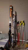 Full view of skis and poles against wall, showing two pairs of skis and two pairs of poles