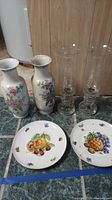Full set of 2 vases, 2 glass candle holders, and 2 fruit design plates on tiled floor.