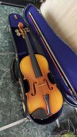 Full view of the child's violin in its open hard case with blue interior lining, showing violin and bow.