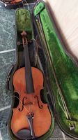 Wooden violin in green velvet-lined case with violin bow, showing overall condition and storage method.