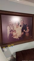 Large family portrait in a wooden frame with a purple background, showing six people of various ages.