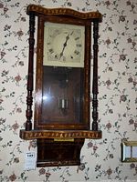 Front view of the antique wooden wall clock hanging on floral wallpapered wall.