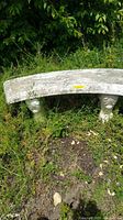 Full view of a curved concrete bench with detailed edges and sculpted legs placed outdoors on grass.