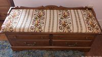 Top view showing the padded floral upholstered top of the cedar chest bench with carved wooden frame and brass handles.