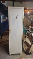 Front full view of white metal tall cabinet with visible dirt marks and stickers adhered to front door.