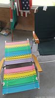 Two folding beach chairs displayed: one with dark green fabric and wooden armrests, another with multicolor striped fabric and wooden armrests, both with metal frames.