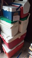 Stack of 6 coolers including blue, white, green, red, and white with red lid, in garage setting.