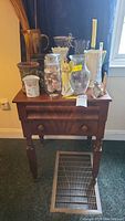 Front view of wooden end table with assorted decorative items on top, showing drawer with wooden knobs and turned legs.