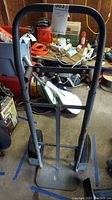 Front view of metal 4-wheeled hand truck showing frame, wheels, and handle in a garage environment.