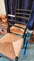 Side and front view of one black wooden framed chair with rush woven seat, showing the woven seat detail and horizontal back slats.