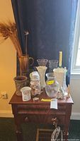 Full view of the lot showing various vases, figurines, and decorative jar with seashells arranged on a wooden table against a dark backdrop with wheat stalks in vase.