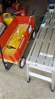 Radio Flyer wagon, red paint, wooden interior, white wheels, with some cords inside, next to the scaffold stand