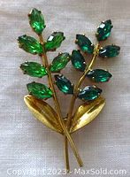 Front view of the brooch showing two stems with prong set light green and emerald marquise glass stones, gold tone leaves at the base.