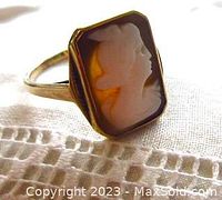Close up image of the rectangular cameo carved from shell in yellow gold ring. Shows carved profile woman's face in white relief against dark background.