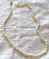 Full view of the cultured freshwater pearl necklace laid out on a white cloth surface highlighting the pearl strand and clasp.