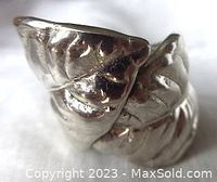 Close-up photo of the front side of a chunky sterling silver ring with two large leaf designs embossed across the top.