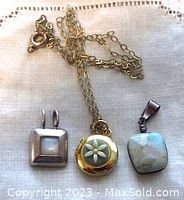 Top view of three pendants and chain: square mother of pearl pendant in silver-tone metal, gold-filled floral locket on chain, and Larimar stone pendant in silver-tone metal.