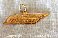 Front view of the gold charm shaped like the state of Tennessee with 'TENNESSEE' embossed on it.