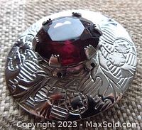 Front detail showing large faceted deep purple amethyst glass stone set in silver tone metal with detailed Celtic engraving around edges.