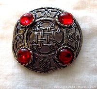 Front view of a round vintage brooch with Celtic knot design and four red cabochon glass stones on a pewter finish metal base.
