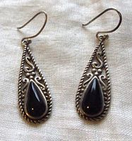 Front view of both earrings showing black teardrop stones framed by ornate sterling silver pierced work and rope border on a white fabric background.