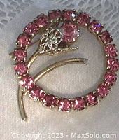 Front side showing the gold-tone metal circular brooch with prong-set lighter pink rhinestones forming a circle and a flower with pierced petals and a larger multi-prong set pink stone in the center.
