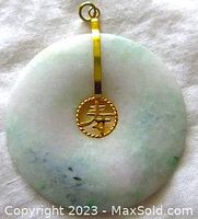 Front view of the round mottled green and white jade pendant with gold plated setting and circular charm showing Asian character detail